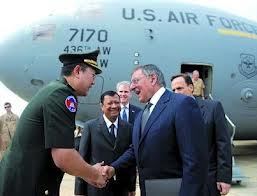 A photograph showing a Cambodian military official shaking hands with a Western diplomat in front of a U.S. Air Force aircraft.