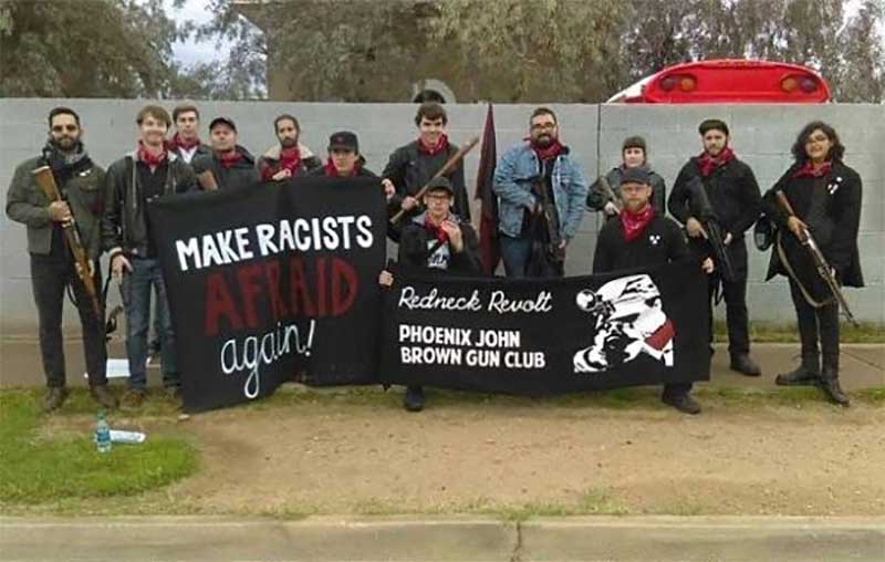 A group of armed individuals from the Redneck Revolt Phoenix John Brown Gun Club standing behind banners that read 'MAKE RACISTS AFRAID AGAIN!' and 'Redneck Revolt PHOENIX JOHN BROWN GUN CLUB'.