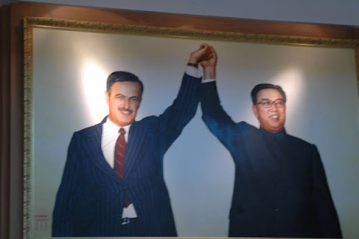 A framed portrait of Syrian President Hafez al-Assad and North Korean leader Kim Il Sung holding their joined hands high in a sign of alliance.