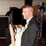 A photograph of a man in a black suit and white shirt smiling at a woman in a white dress whose face is covered by a black rectangle.
