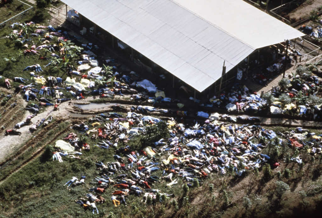 An aerial photograph showing the aftermath of the Jonestown massacre, with hundreds of bodies lying on the ground surrounding a large pavilion building in Guyana.