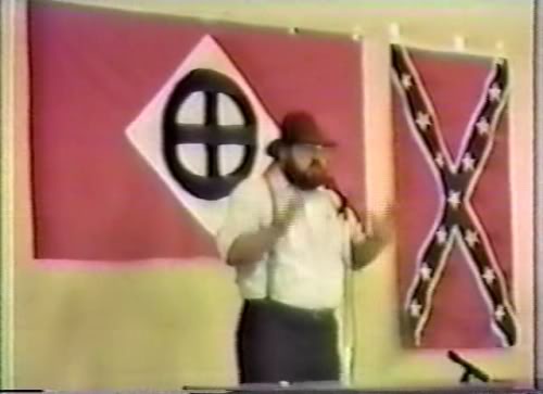 Northwest Front leader Harold Covington, a far right wing neo Nazi White Supremacist who was an ideological source for church shooter Dylann Roof. Note the symbol on the flag behind Covington, which Roof drew in the sand in a photo he posted on his website