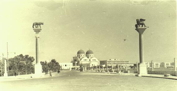 A vintage black and white photograph of a city square in Benghazi, Libya, featuring two tall columns with statues on top and a domed building in the background.