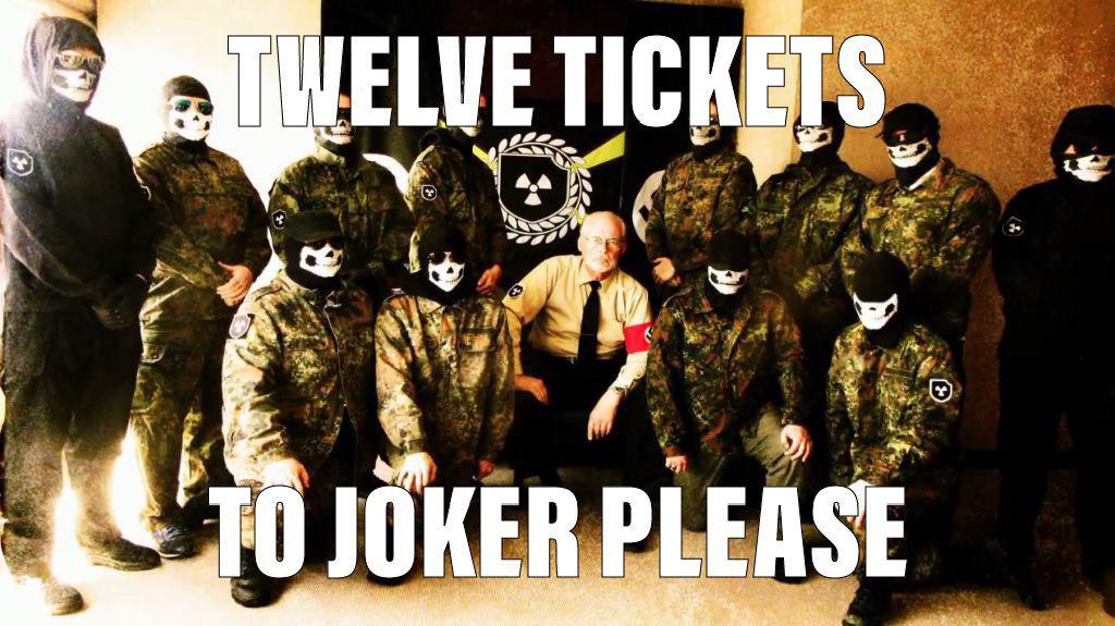 A group of men in camouflage and black tactical gear wearing skull masks, surrounding an older man with white hair and a mustache wearing a tan shirt, black tie, and a red armband. Large white text overlays the image reading 'TWELVE TICKETS TO JOKER PLEASE'.