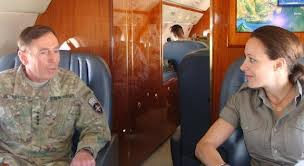 General David Petraeus in military uniform speaking with Paula Broadwell inside an aircraft cabin.
