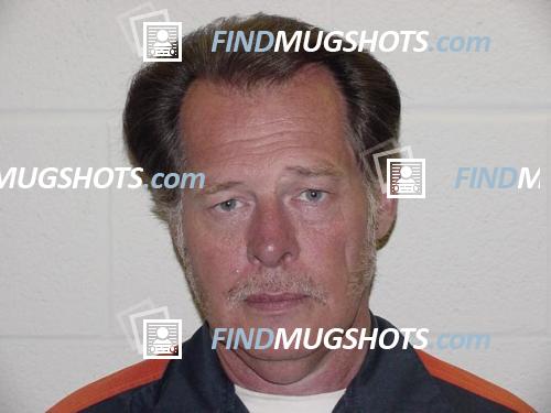 A mugshot of a middle-aged Caucasian man with brown hair, a mustache, and sideburns, wearing a blue and orange jacket.