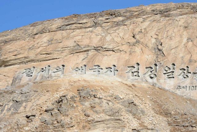 A large-scale North Korean propaganda slogan carved into a rocky mountainside, featuring prominent Korean characters.