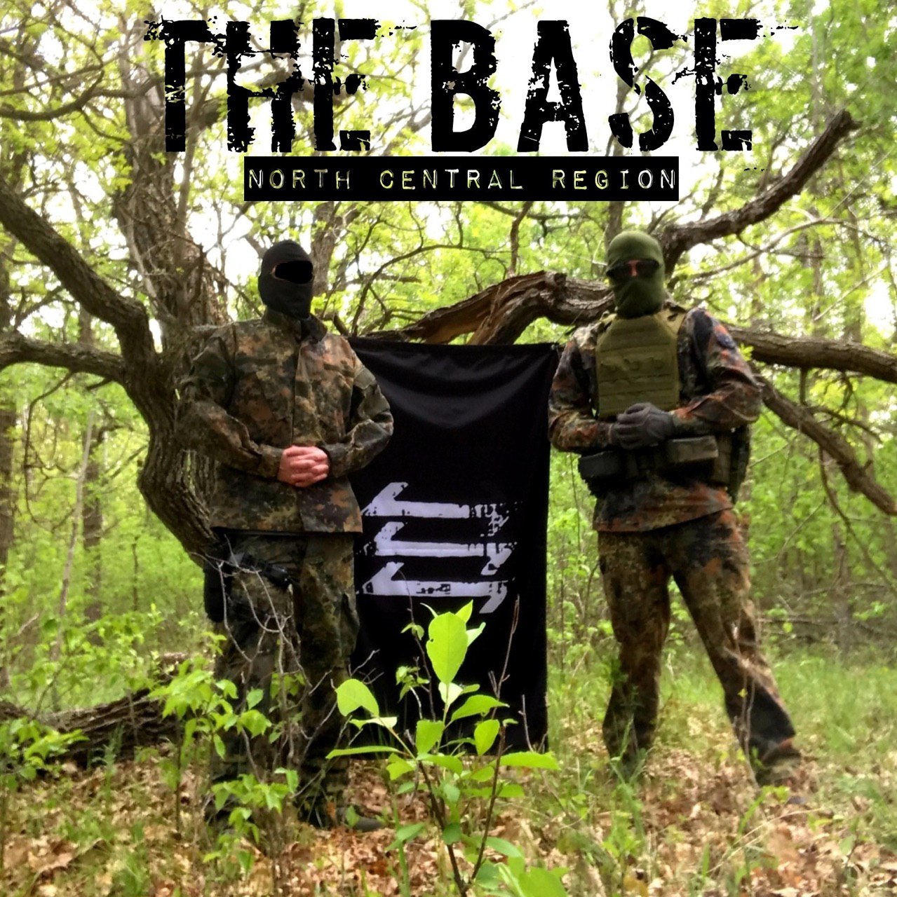 Two individuals in camouflage uniforms and full-face masks stand in a forest next to a black flag with a white logo. Text overlay reads 'THE BASE NORTH CENTRAL REGION'.