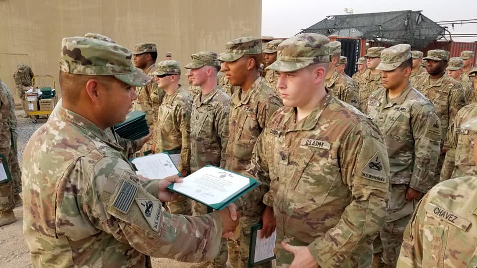 A group of US Army soldiers in camouflage uniforms standing in formation. One soldier, with the name tag 'CARVER', is receiving a certificate from another soldier during a ceremony.