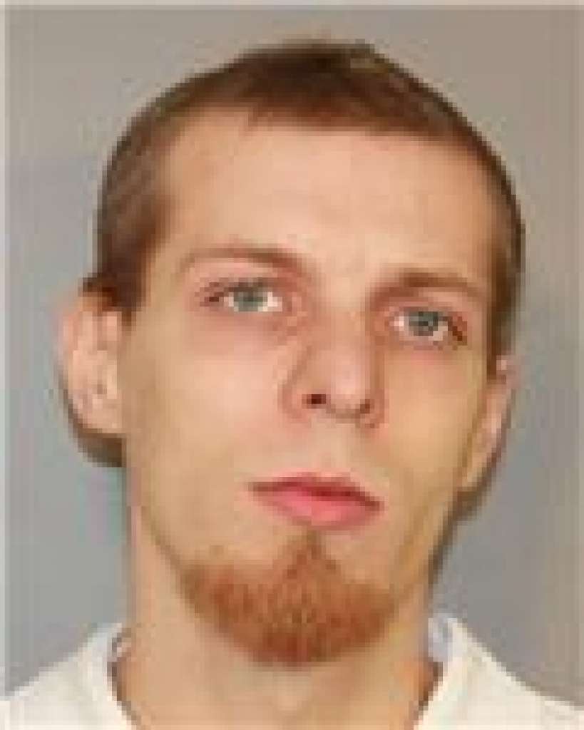 A low-resolution mugshot-style photograph of a young Caucasian man with short brown hair and a reddish-brown goatee.