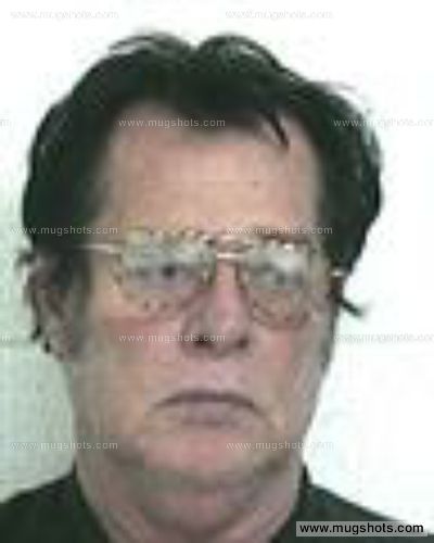 A mugshot of a Caucasian man with dark hair and glasses, featuring watermarks from mugshots.com.