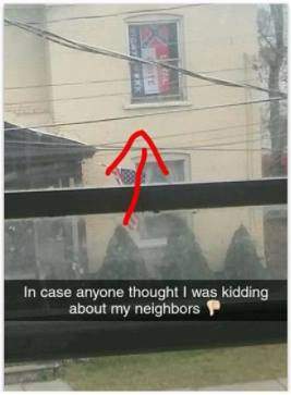 A photograph taken from across a street showing a two-story building. A red arrow points to a second-story window where a Confederate flag and a banner for the 'Loyal White Knights' of the KKK are displayed. A caption at the bottom reads, 'In case anyone thought I was kidding about my neighbors 👎'.